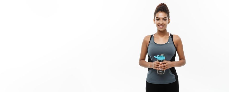 Healthy and Fitness concept - beautiful African American girl in sport clothes holding water bottle after workout. Isolated on white studio background.