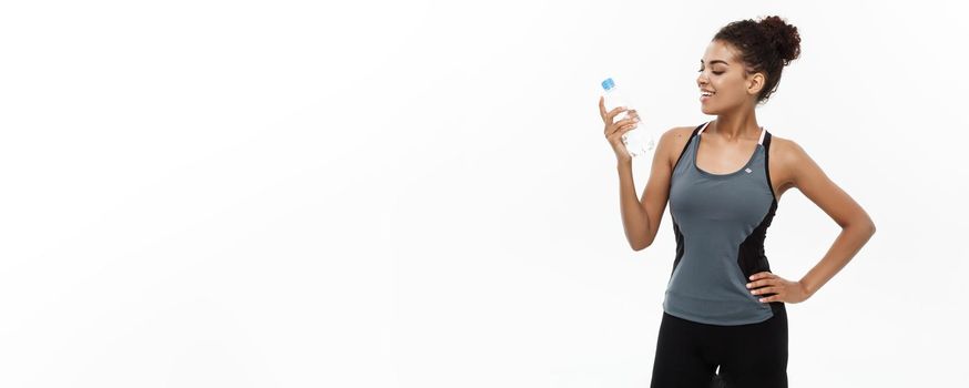 Healthy and Fitness concept - beautiful African American girl in sport clothes holding plastic water bottle after workout. Isolated on white studio background.