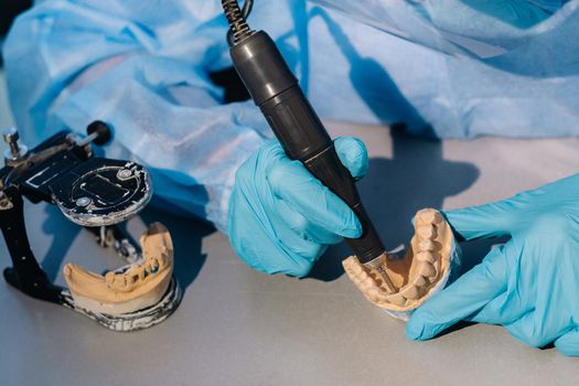 A masked and gloved dental technician works on a prosthetic tooth in his lab.