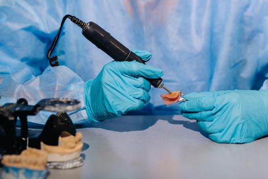 A masked and gloved dental technician works on a prosthetic tooth in his lab.