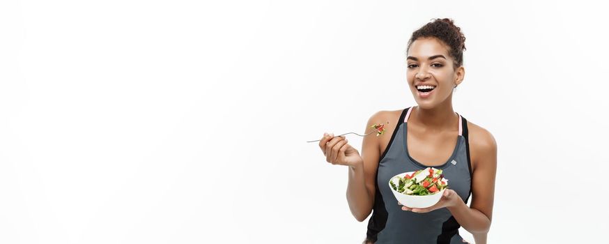 Healthy and Fitness concept - Beautiful American African lady in fitness clothes on diet eating fresh salad. Isolated on white background