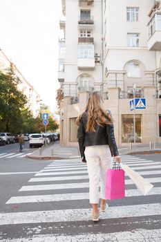 Vertical full length shot of unrecognizable woman crossing the road in the city, carrying shopping bags