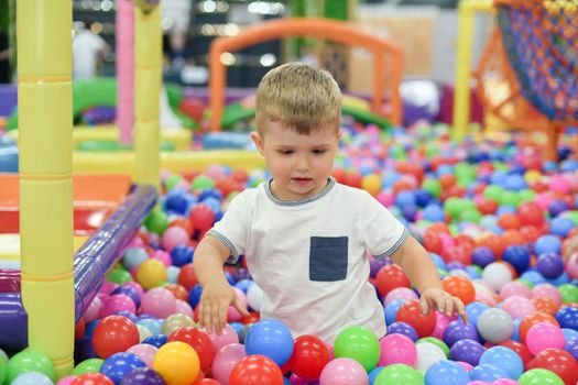 A cut boy in a dry paddling pool in playing centre with plastic balls.