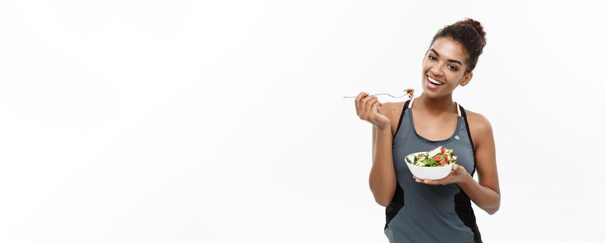 Healthy and Fitness concept - Beautiful American African lady in fitness clothes on diet eating fresh salad. Isolated on white background