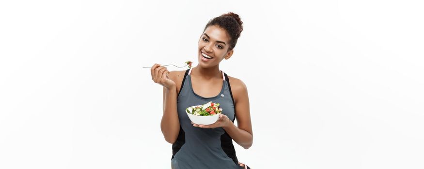 Healthy and Fitness concept - Beautiful American African lady in fitness clothes on diet eating fresh salad. Isolated on white background