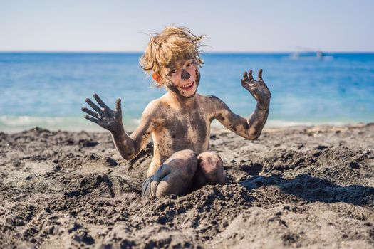 Black Friday concept. Smiling boy with dirty Black face sitting and playing on black sand sea beach before swimming in ocean. Family active lifestyle, and water leisure on summer vacation with kids. Black Friday, sales of tours and airline tickets or goods.