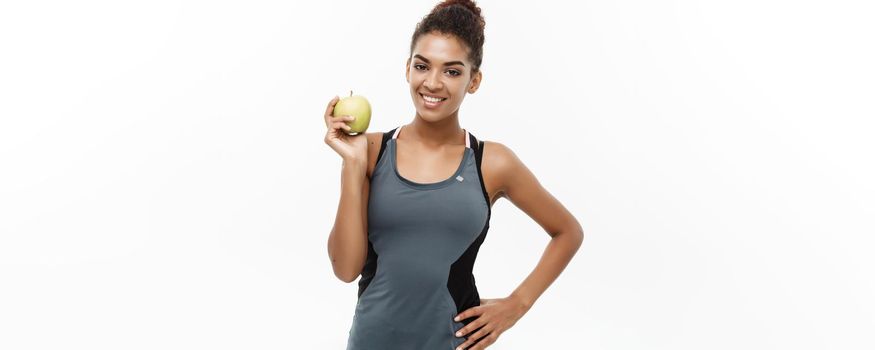 Healthy and Fitness concept - Beautiful American African lady in grey fitness clothes holding green apple. Isolated on white background