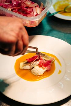 Arranging a dish in a restaurant in Venice. Sea bass steak in yellow stew with caramelized onions.