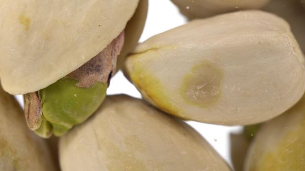 Pistachios in shells fall on glass against a bright white background. Pistachios macro bottom view. 4k