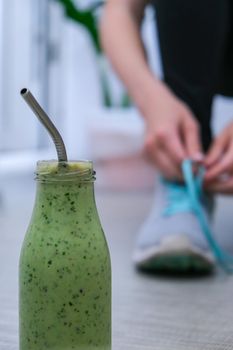 Seasonal Matcha green vegan smoothie with chia seeds and mint smoothie drink detox. Woman ties shoelaces on background Clean eating, weight loss, healthy dieting food concept. Fitness training workout at home.