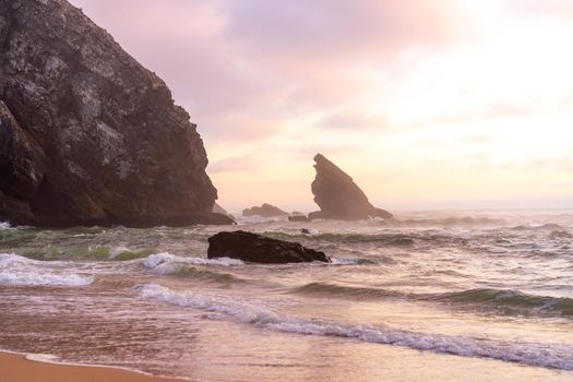 Sunset on the Ocean wild beach stormy weather. Praia da Adraga sandy beach with picturesque landscape background, Sintra Cascais Portugal Vitality of blue energy and clear ocean water