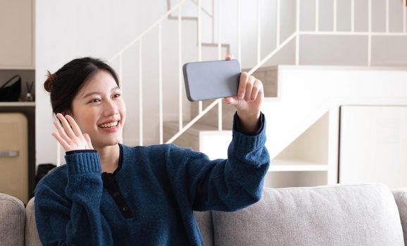 Portrait beautiful young asian woman use smart mobile phone on sofa in living room interior.