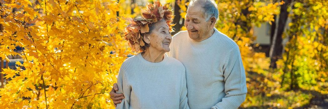 Happy old couple having fun at autumn park. Elderly man wearing a wreath of autumn leaves to his elderly wife. BANNER, LONG FORMAT