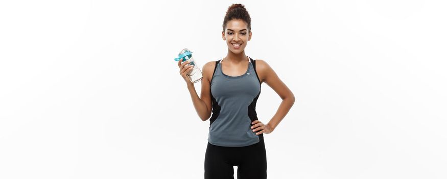 Healthy and Fitness concept - beautiful African American girl in sport clothes holding water bottle after workout. Isolated on white studio background.