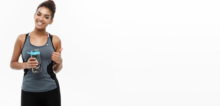 Healthy and Fitness concept - beautiful African American girl in sport clothes holding water bottle after workout. Isolated on white studio background.