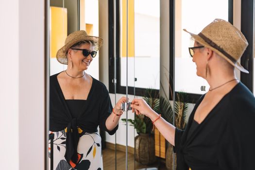 happy mature woman looking at her summer look in front of the wardrobe mirror. tourist in hotel enjoying her trip.. bedroom, natural light, dressing room with mirrors.