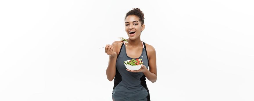 Healthy and Fitness concept - Beautiful American African lady in fitness clothes on diet eating fresh salad. Isolated on white background