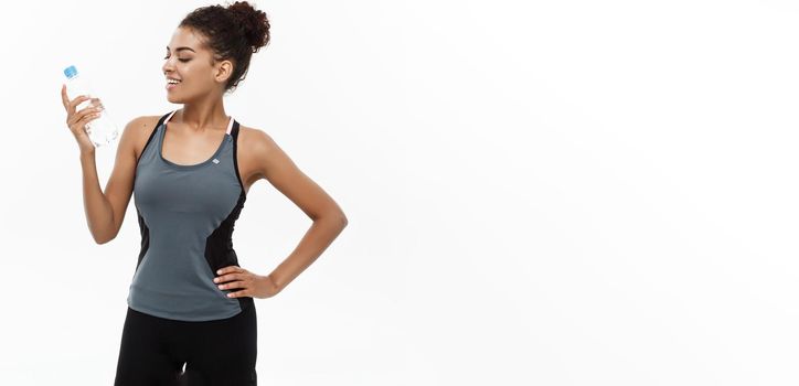 Healthy and Fitness concept - beautiful African American girl in sport clothes holding plastic water bottle after workout. Isolated on white studio background.