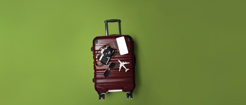 Flat lay suitcase with sunglasses, smart phone and camera on green background. Holidays, travel, tourism, flight luggage concept.