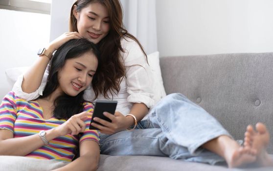 Young beautiful Asian women lesbian couple lover using smartphone video call online in living room on sofa at home with smiling face.Concept of LGBT sexuality with happy lifestyle together..