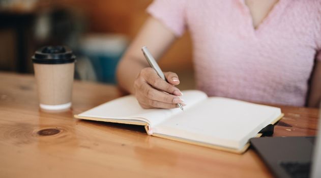 Cropped photo of woman writing making list taking notes in notepad working or learning on laptop indoors- educational course or training, seminar, education online concept.