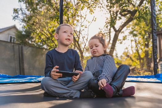 children look at the phone while sitting on a trampoline