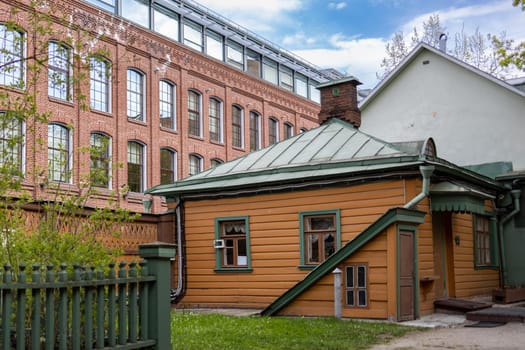 An old wooden manor house on the background of a modern office building made of red brick. A clear sunny day with a blue sky with clouds. High quality photo