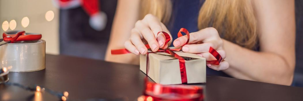 Young woman is packing presents. Present wrapped in craft paper with a red and gold ribbon for christmas or new year. Woman makes an advent calendar for her child. BANNER, LONG FORMAT