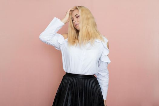 Beauty, fashion portrait. Elegant business style. Portrait of a beautiful blonde woman in white blouse and black skirt posing at studio on a pink background.