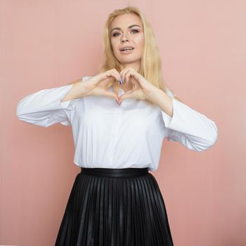 Beauty, fashion portrait. Elegant business style. Portrait of a beautiful blonde woman in white blouse and black skirt posing at studio on a pink background.