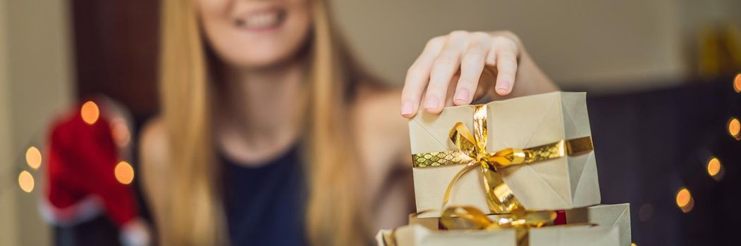 Young woman is packing presents. Present wrapped in craft paper with a red and gold ribbon for christmas or new year. Woman makes an advent calendar for her child. BANNER, LONG FORMAT