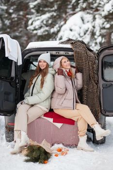 Two girls in love sitting in a car in a winter forest. Girls smile, and laugh