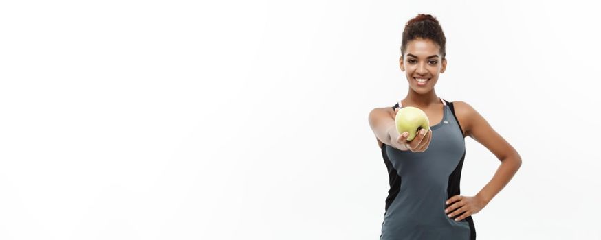 Healthy and Fitness concept - Beautiful American African lady in grey fitness clothes holding green apple. Isolated on white background