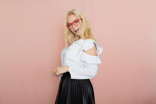 Beauty, fashion portrait. Elegant business style. Portrait of a beautiful blonde woman in white blouse and black skirt posing at studio on a pink background. Wearing red glasses