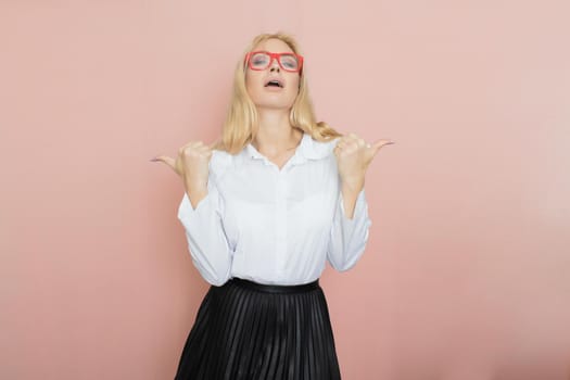 Beauty, fashion portrait. Elegant business style. Portrait of a beautiful blonde woman in white blouse and black skirt posing at studio on a pink background. Wearing red glasses