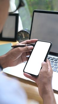 Close up over shoulder view of young man using mobile phone in home office.