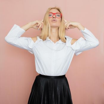 Beauty, fashion portrait. Elegant business style. Portrait of a beautiful blonde woman in white blouse and black skirt posing at studio on a pink background. Wearing red glasses