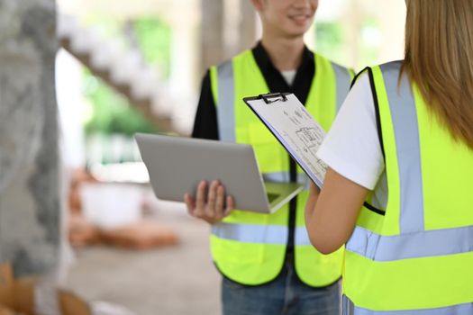 Two architects wearing uniform and safety helmet inspecting industrial building construction site. Industry, Engineer, construction concept.