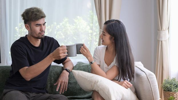Relaxed young couple sitting on sofa and drinking hot coffee, spending morning time together at home.