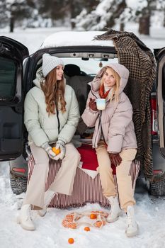 Two girls in love sitting in a car in a winter forest. Girls smile, and laugh