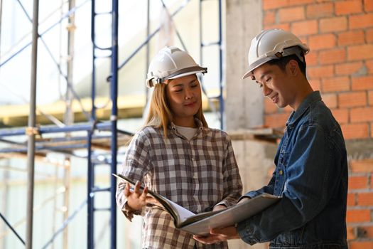 Two architects wearing safety helmet working on blueprints at construction site.