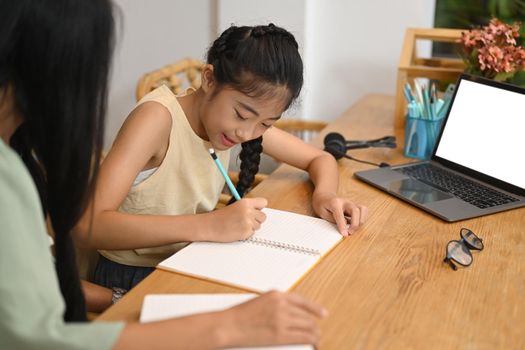 Happy asian girl doing assignments with her mother in home kitchen.