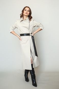 The girl is a model in a coat dress with a leather belt. Studio background.