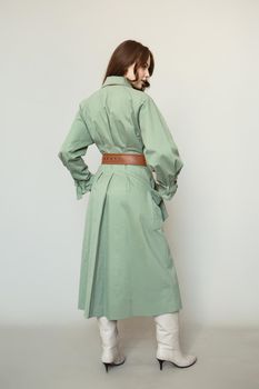 A model in a green coat with a brown leather belt.