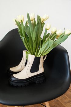 Fashionable shoes that stand on a chair. There are tulips in the shoes.