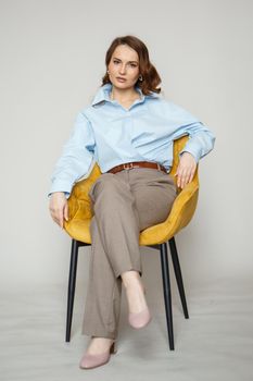 A girl in a blue shirt and trousers is sitting on a yellow chair.
