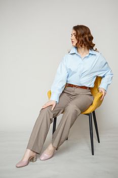 A girl in a blue shirt and trousers is sitting on a yellow chair.
