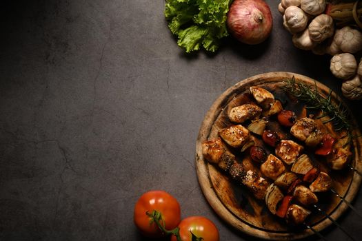 Barbecued chicken kebab with bell pepper, cherry tomato and onions on dark stone background. Copy space for your text.