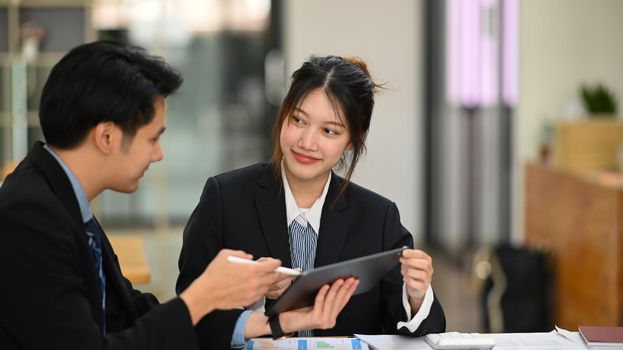 Two young employees working and discussing project strategy at co working space.