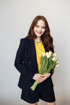 A model girl is standing in a studio with flowers. In the hands of a beautiful girl tulips.